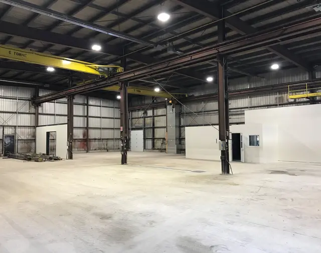 Renovated high-bay interior with a yellow overhead crane and new white office enclosure