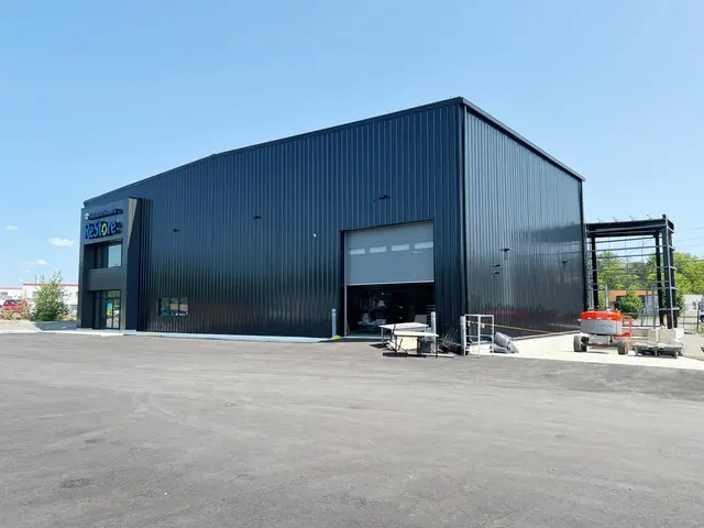 Renovated building in dark ribbed metal cladding with a new glazed entrance and overhead loading door