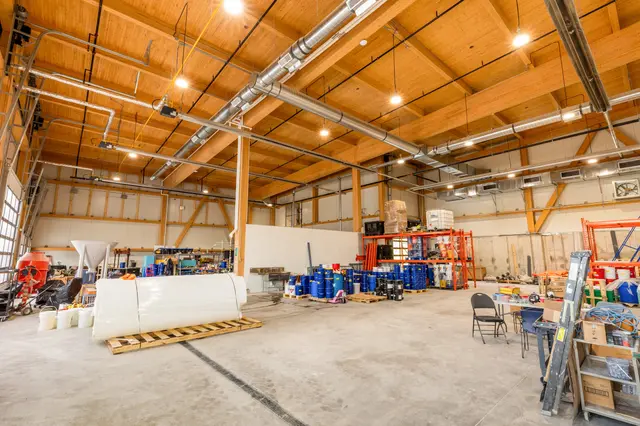Warehouse interior under an exposed glulam roof structure, with equipment and storage racks