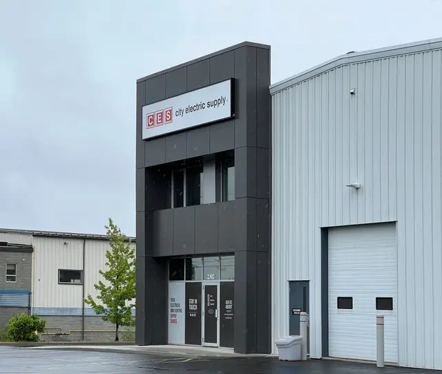 New dark grey entrance volume with a tenant sign, set against the building's light metal cladding