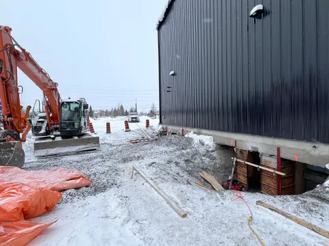 Excavator beside the building in winter during foundation underpinning for the loading ramp
