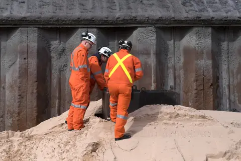 Two workers in orange coveralls inspecting a slag block